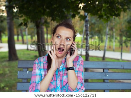 Portrait of surprised beautiful woman in the park talking on the phone