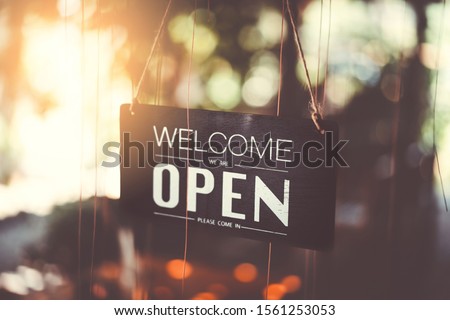 Wooden open sign hanging on tree front of cafe with green nature bokeh sunlight background. Business finance and service concept. Vintage tone filter effect color style.