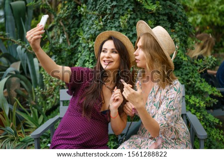two cheerful friends take a selfie on the phone on the background of the Botanical garden