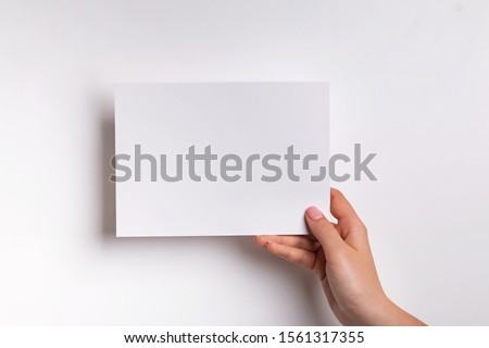 Woman hand holding sheet of paper against white wall