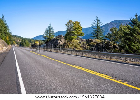 A mesmerizing landscape that attracts tourists with a straight road with road sign around a rock cliff on one side and an abyss on the other side in the autumn forested mountains of Columbia Gorge 