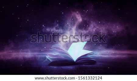 An open book on a wooden table under the night sky against a dark forest. Magical radiance. Night scene. Royalty-Free Stock Photo #1561332124