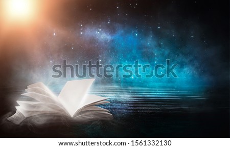 An open book on a wooden table under the night sky against a dark forest. Magical radiance. Night scene.