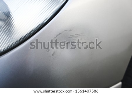 Close up of small dent and scratches on silver gray car. Car with damage from crash accident, parking lot or traffic. Royalty-Free Stock Photo #1561407586