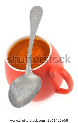 Mug of homemade pumpkin soup with a spoon in closeup on white background