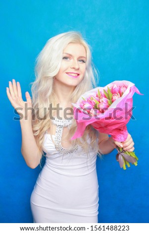 hot happy kind woman in white tight fashion dress with pink tulip flowers on blue studio background.