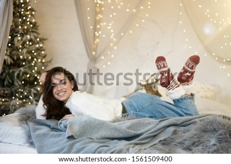 Young beautiful smiling woman wearing christmas sweater and socks in a room decorated for celebrating the new year and christmas festive mood