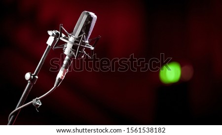Recording light on green. Shallow focus on a stand mounted condenser microphone with a green recording light showing in the background blur.