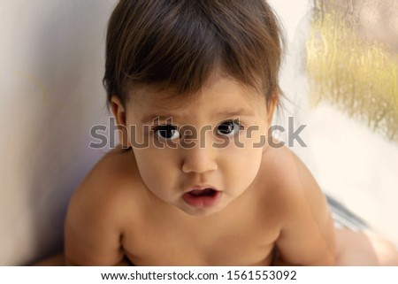 A baby girl with innocent face, The child sits sad on the windowsill