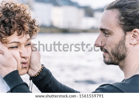 Stock photo of a young boy who plays with his partner's cheeks with the background sea out of focus. Lifestyle