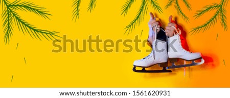 Hands hold the winter skates by the laces. They protrude from a hole in the yellow paper background and are illuminated by neon light