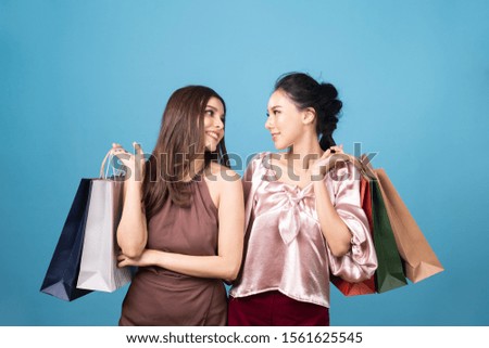 Young pretty cute two Asian woman holding shopping bags in both hands with smiley face standing in studio. Girl wearing hat and dress in summer style costume. Happy shopping in summer sale concept.