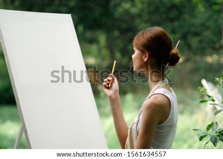 young woman outdoors paints a picture on canvas