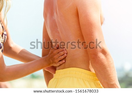 caucasian couple on the beach woman concentrates sun protection cream to man, woman smears sun UV cream on the beach on a mans back