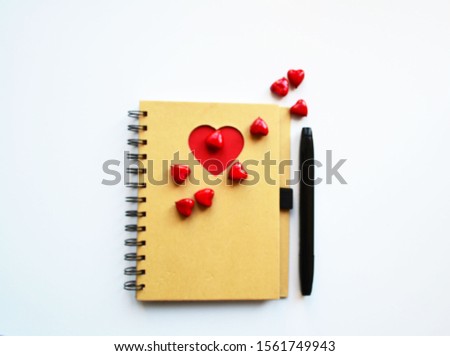 red hearts are scattered over the notebook next to the black pen