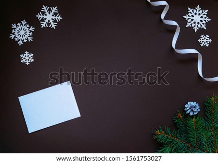 Christmas composition. Paper blank, christmas tree branches, white decorations on dark background. Luxury New Year post card. Flat lay, top view, copy space.