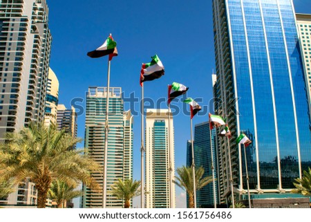 View of Dubai buildings with UAE flags. United Arab Emirates flags waving on blue sky background. Independence day. UAE flags on street. Flag day