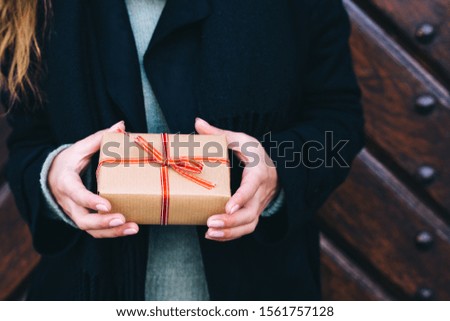 Woman giving a christmas or birthday gift wrapped in brown paper and red ribbon. Copy space. Wood old background.