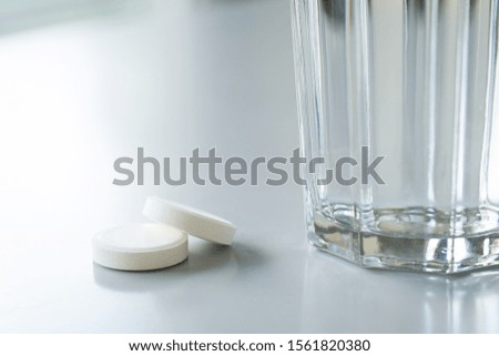 Two white tablets on table near glass with water. Ill person is ready to take pills