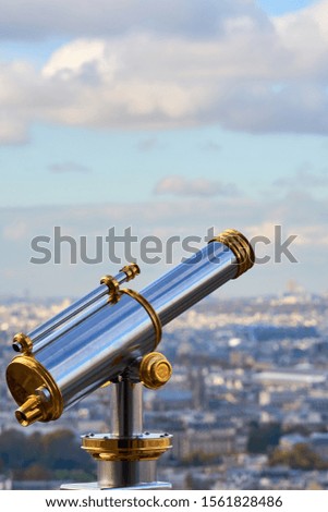          Telescope with blurred city of Paris, France on a background and blue sky with clouds. Copy space.