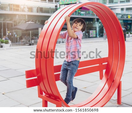 HIgh key portrait of happy little boy standing on red chair, Adorable child playing with outdoor metal chair in sunny day summer, Kid playing outside, Positive children concept