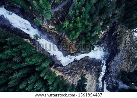 A breathtaking high angle shot of a waterfall on a rock surrounded by a forest of beautiful tall spruces