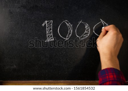 Hand writes the number 1000 of subscribers on the board.