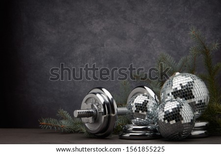 Sports equipment (dumbbell with weights), fir branch, Christmas ornament on dark grey background with copy space. Fitness, sport or healthy lifestyle concept. New Year and Christmas.