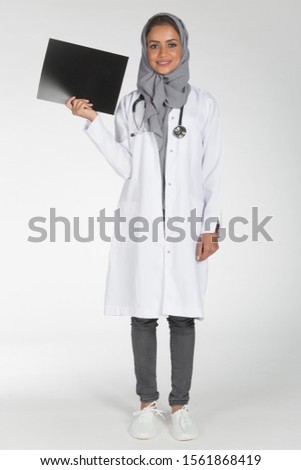 Young Saudi female doctor wearing doctor uniform and Hijab and Stethoscope in various positions, expresseions and hand gestures on white isolated background.