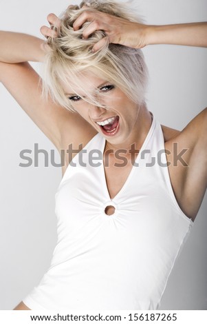 Attractive young woman throwing a tantrum or having a rave standing shouting with her hands raised to her tousled blond hair