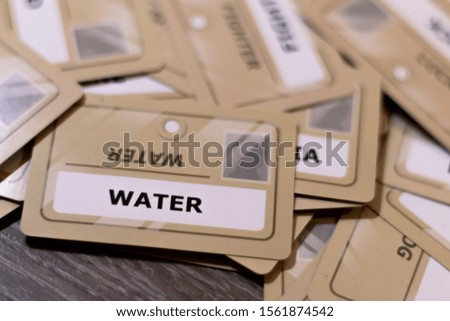Water word on a yellow card, shallow depth of field. Multiple cards visible out of focus. Concept of polluted water, draughts, life and death.