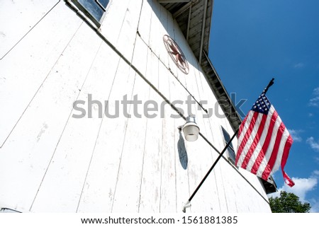 American flag hanging on old white country barn united states, blue sky background