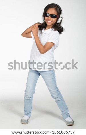 Arab Saudi cute girl wearing jeans and white shirt, wearing headphones, dancing and jumping against white isolated background.