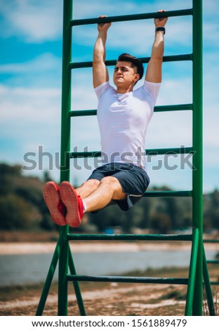 Sportsman with  in black pants doing exersices on horizontal bar in a outdoor gym