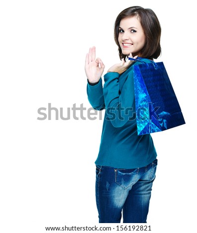 Attractive young woman in a blue shirt. Holds the gift bag and showing sign of okay. Isolated on white background