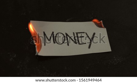 Money word written on white paper burns. Fire with smoke and ashes on black background