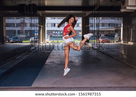 Young beautiful brunette woman jumping in mirror arch of building.