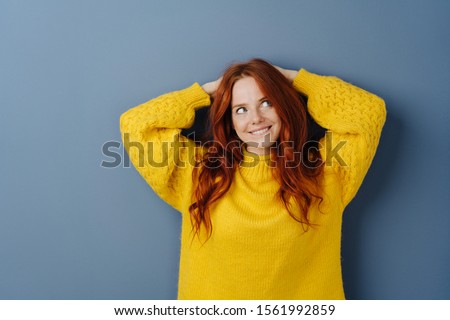 Eager young woman with a look of anticipation and longing looking up with a smile as she makes her plans over a blue studio background with copy space Royalty-Free Stock Photo #1561992859