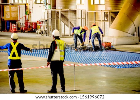 Worker stretching the red white warning tape to the pole at construction site.Red and white Hazardous restricted area tape at construction area of factory to mark territory works and worker inside.