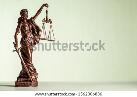 Small bronze statue of Justice with sword and scales wearing a blindfold allegorical of law and order over a pale green background with copy space Royalty-Free Stock Photo #1562006836