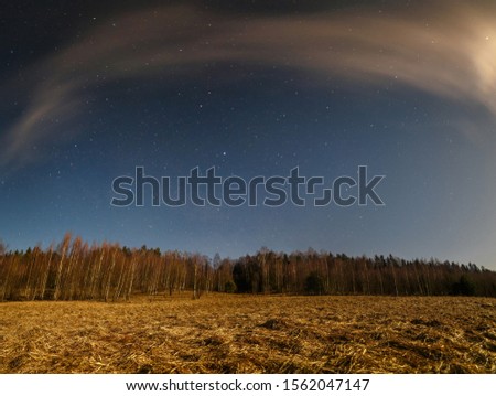 View of the bright autumn night sky over a brown autumn field and forest