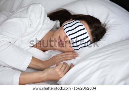Calm serene young woman wear pajamas and sleeping mask resting in comfortable white bed, peaceful healthy beautiful lady lying asleep on soft pillow orthopedic mattress enjoying good sleep concept