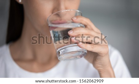 Young beautiful lady holding glass drinking sipping fresh transparent pure filtered mineral water, adult woman hydrating thirst in morning on diet nutrition, healthy lifestyle concept, close up view