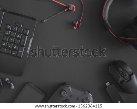 gamer work space concept, top view a gaming gear, mouse, keyboard, joystick, headset and in ear headphone on black table background.