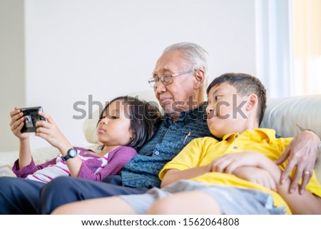 Asian grandfather and grandchildren watching a movie together on a mobile phone at home