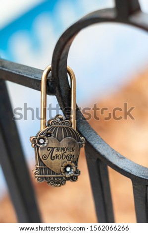 The padlock of the newlyweds with a painted heart with the inscription hangs on the iron structure. (The inscription in Russian-padlock love)
