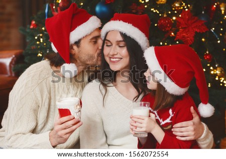 Portrait of lovely happy family bonding on xmas eve, daddy kissing mom, drinking milk