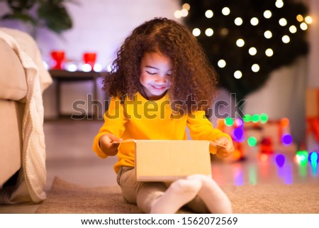 Cheerful little african girl opening Christmas gift box from Santa, empty space
