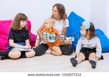 Picture of female teacher playing a guitar with a group of kids in the kindergarten