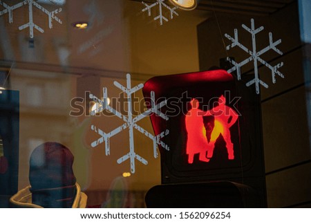 Abstract background with blurry reflections in glass window with scratched white painted snowflakes. Red light of creative traffic lights lamp with fighting people silhouettes. Holiday backdrop
